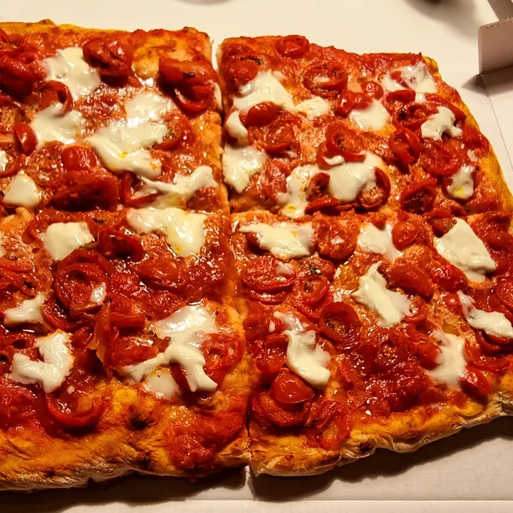 Teglia di pizza rossa con mozzarella, tagliata in quadrati.