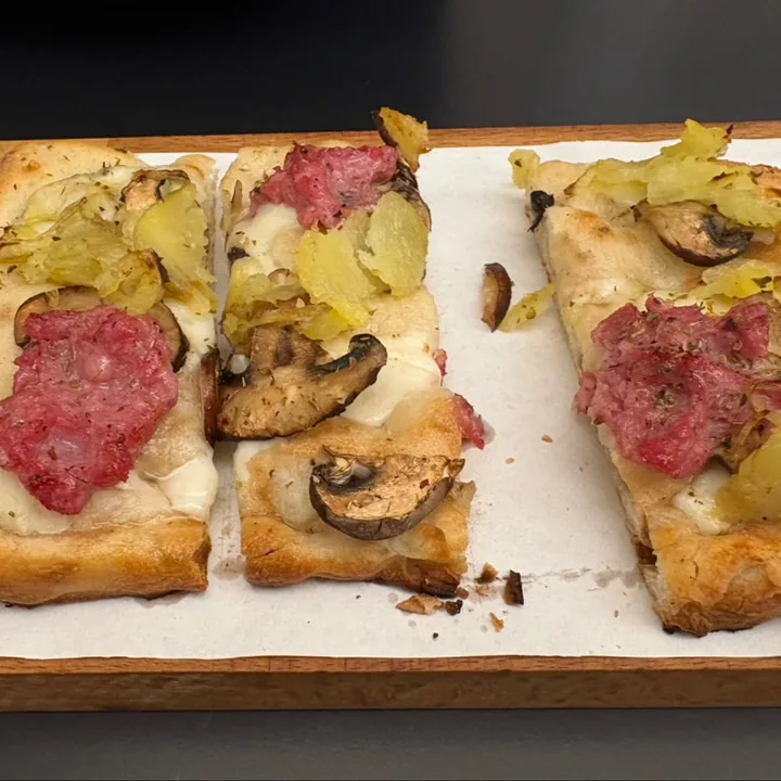 Teglia bianca con patate a fette, salame e funghi.