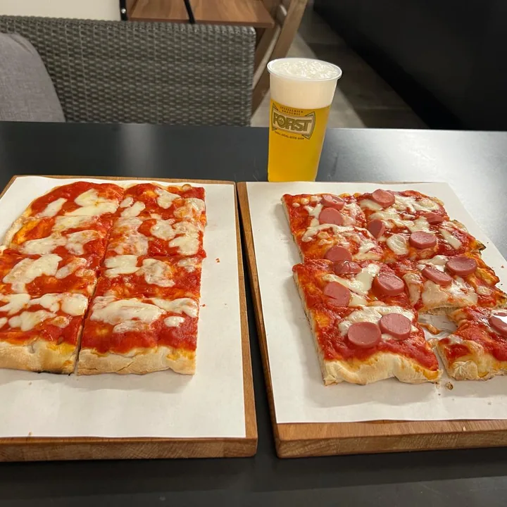 Due tranci di pizza serviti su taglieri di legno, sul bancone alto.